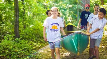 Smiling campers carry canoe on forest path