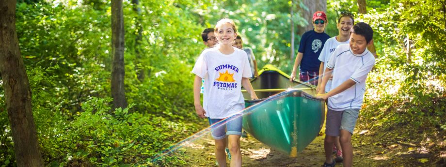 Smiling campers carry canoe on forest path