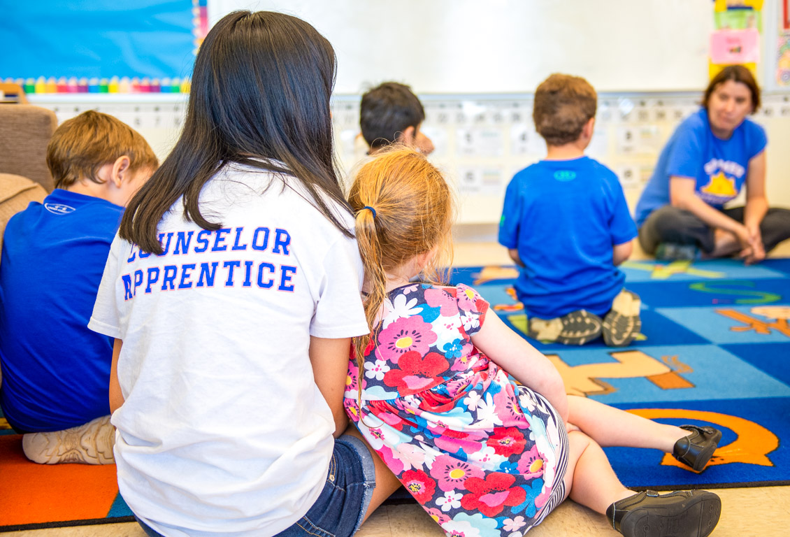 Young camper leans against Counselor Apprentice in classroom